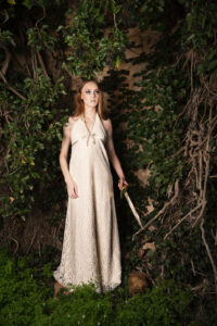 Fine art photography of a woman holding a sword against a backdrop of ivy and sandstone